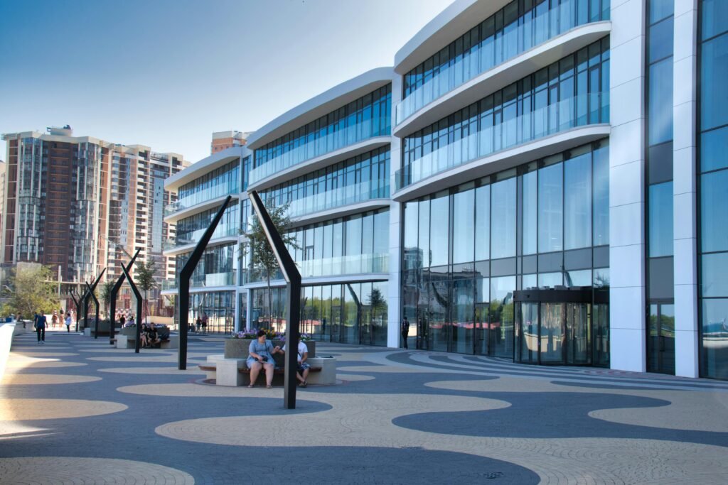 Modern office building with glass panels and outdoor seating in vibrant urban setting.